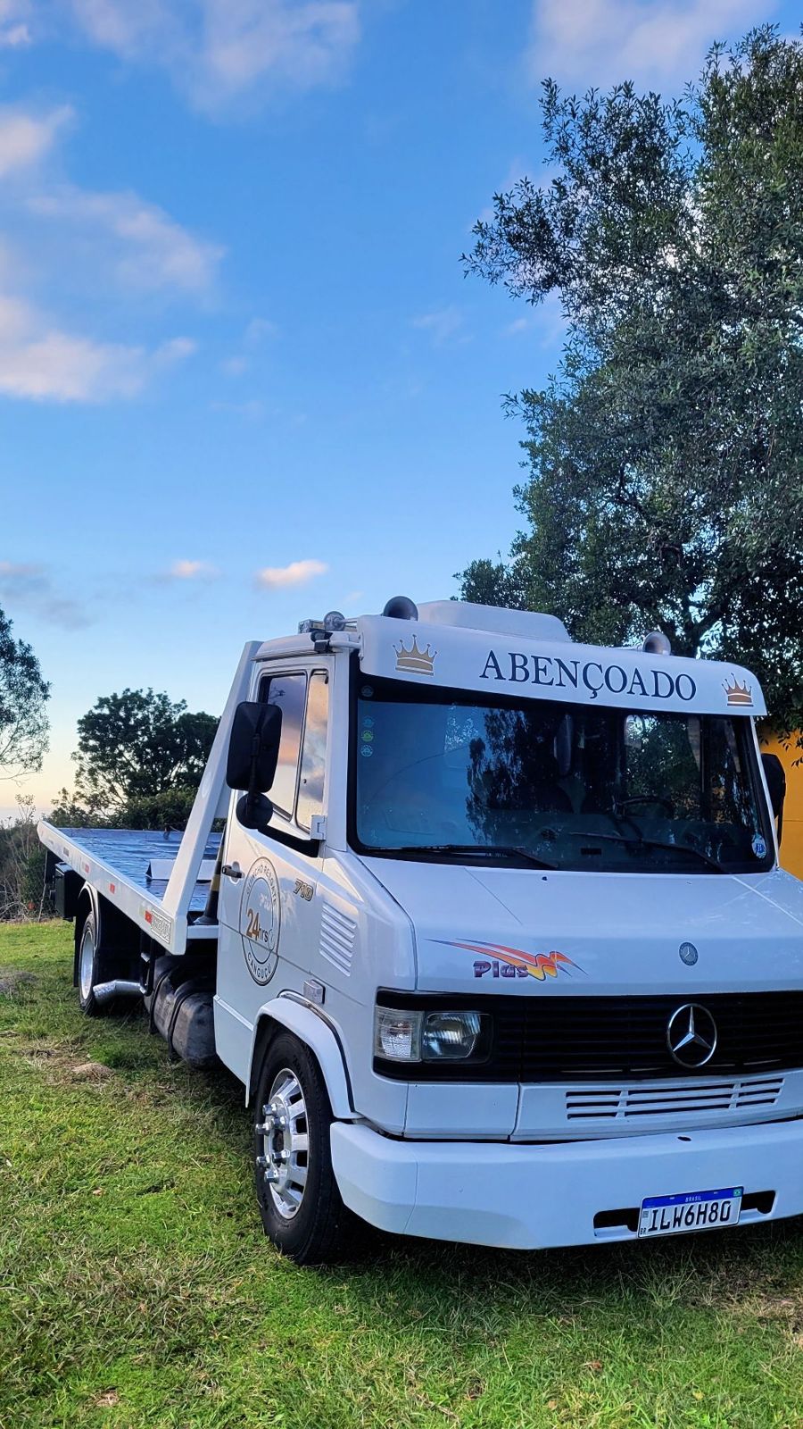 Caminhão guincho plataforma branco com o nome Abençoado na cabine, ao entardecer