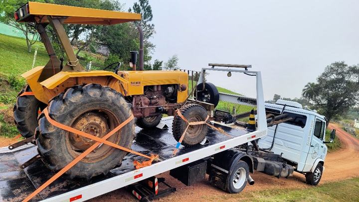Trator amarelo antigo preso com cintas laranja na plataforma